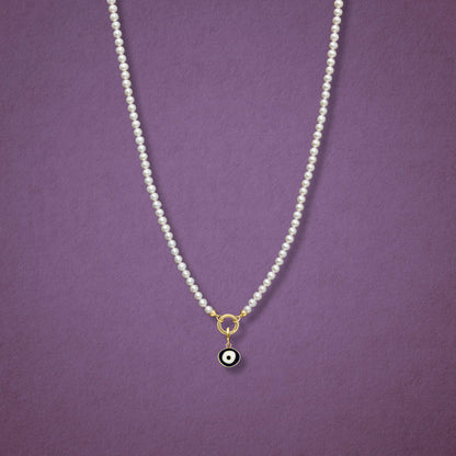 Obsidian Organic Evil Eye Charm with black and white enamel shown on the Lustrous Pearl necklace for scale on a pink background.