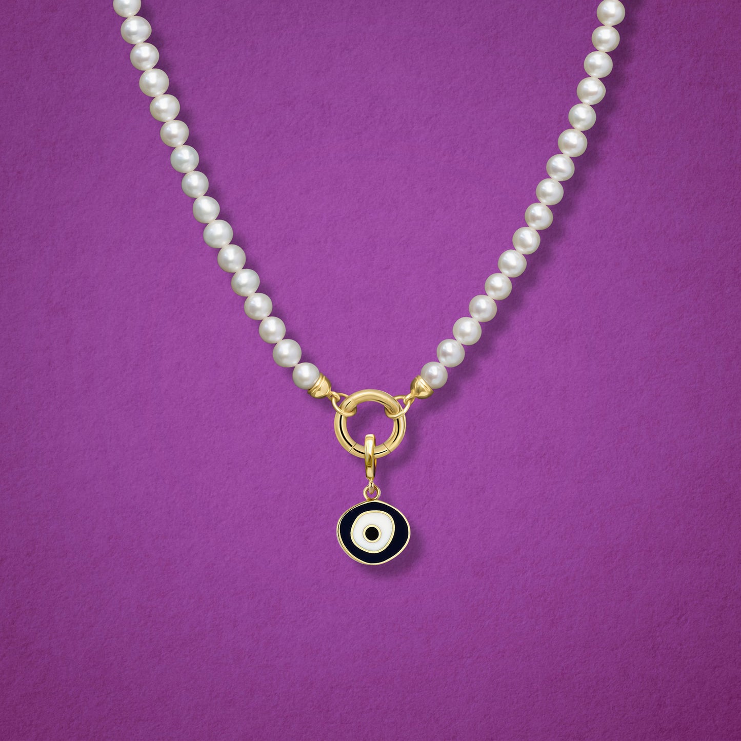 Close-up of the Obsidian Organic Evil Eye Charm with black and white enamel on the Lustrous Pearl necklace, shown on a magenta background.