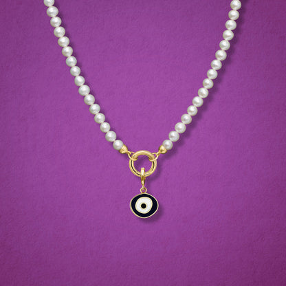 Close-up of the Obsidian Organic Evil Eye Charm with black and white enamel on the Lustrous Pearl necklace, shown on a magenta background.