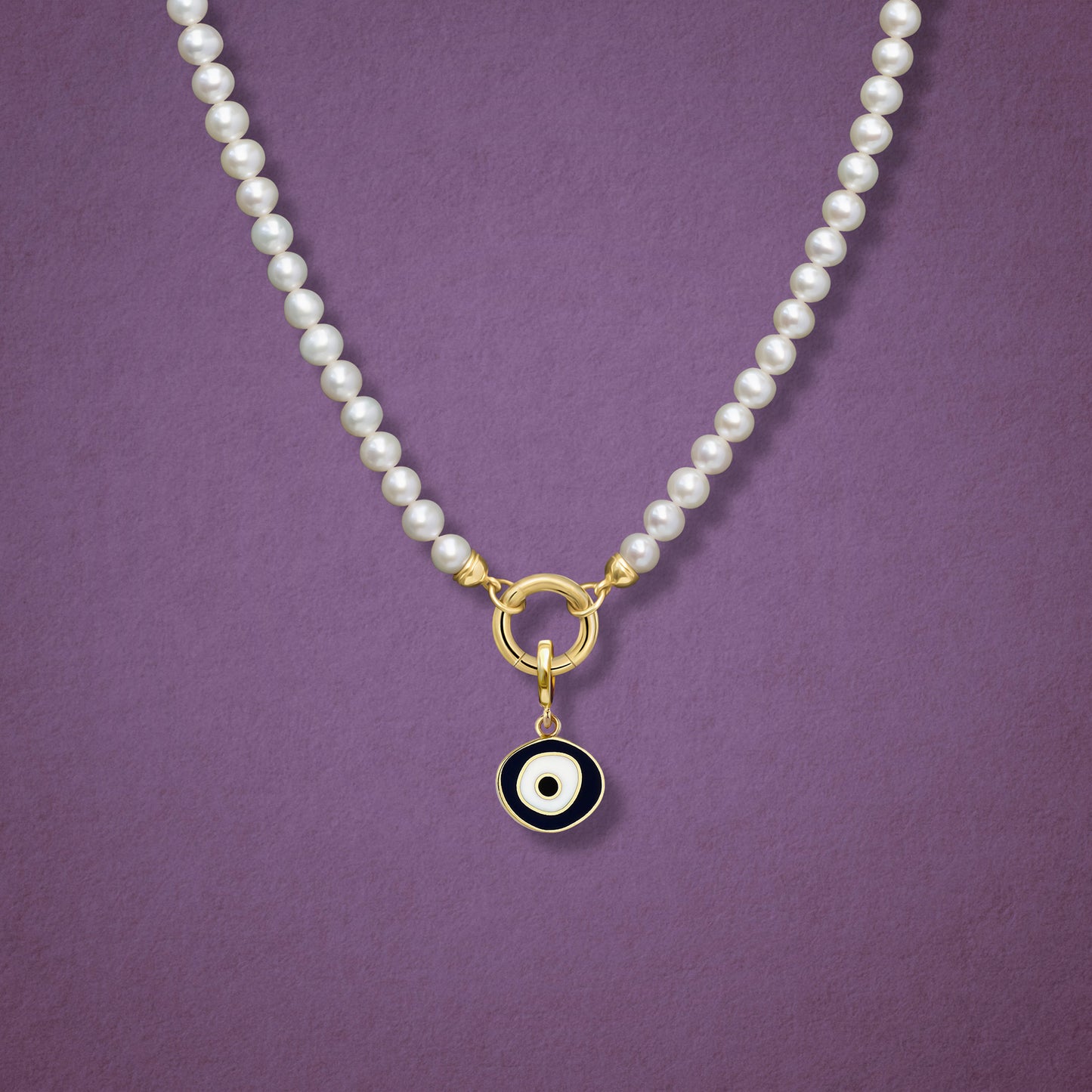 Close-up of the Obsidian Organic Evil Eye Charm with black and white enamel on the Lustrous Pearl necklace, shown on a pink background.