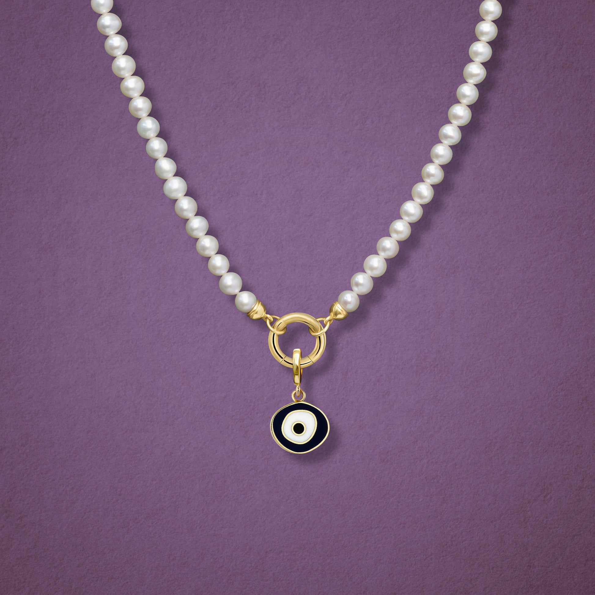 Close-up of the Obsidian Organic Evil Eye Charm with black and white enamel on the Lustrous Pearl necklace, shown on a pink background.