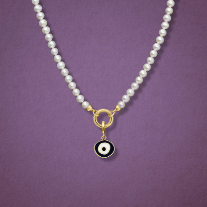 Close-up of the Obsidian Organic Evil Eye Charm with black and white enamel on the Lustrous Pearl necklace, shown on a pink background.