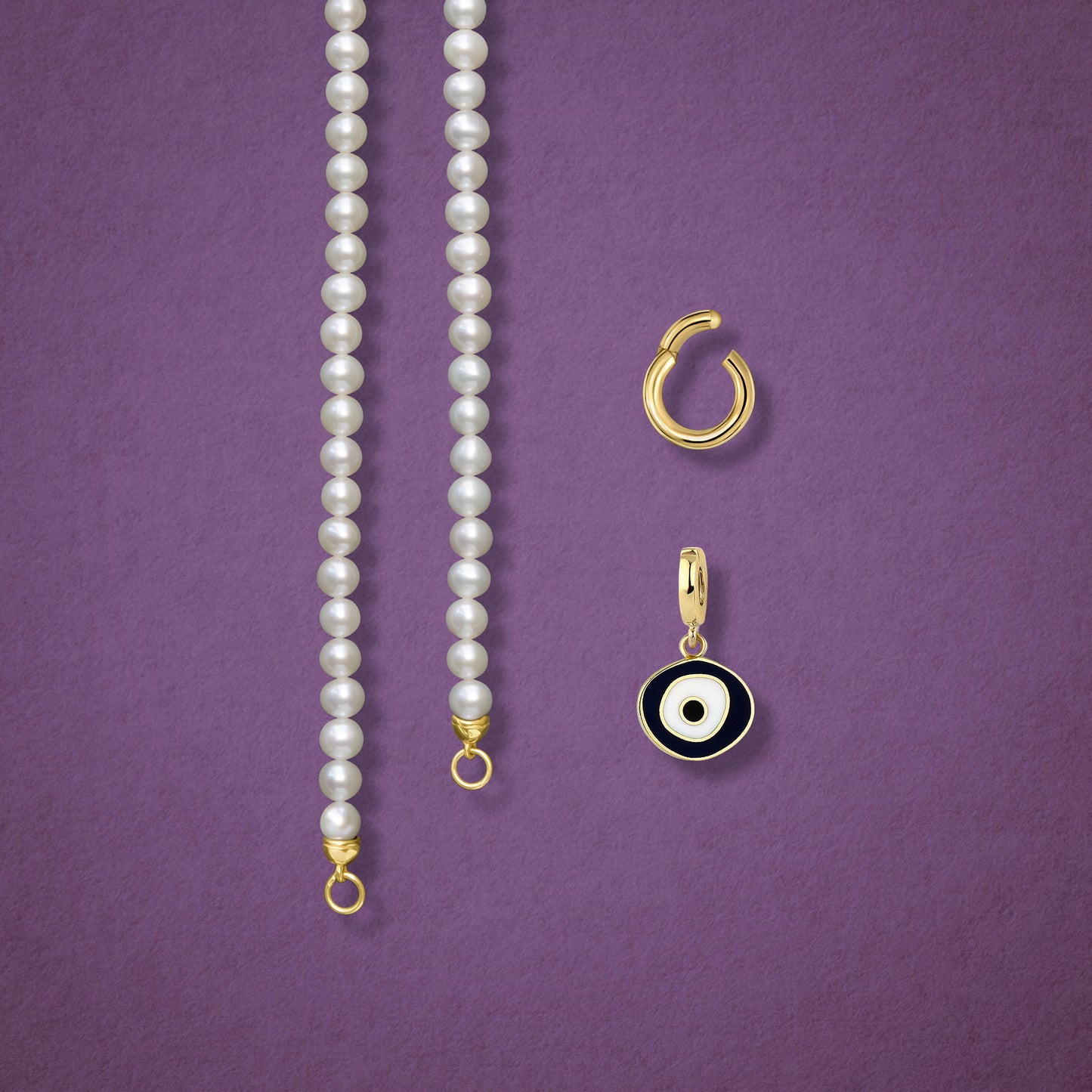 Close-up of the Obsidian Organic Evil Eye clip-on charm, Golden Link Charm Holder, and the Lustrous Pearl necklace displayed side by side on a pink background.