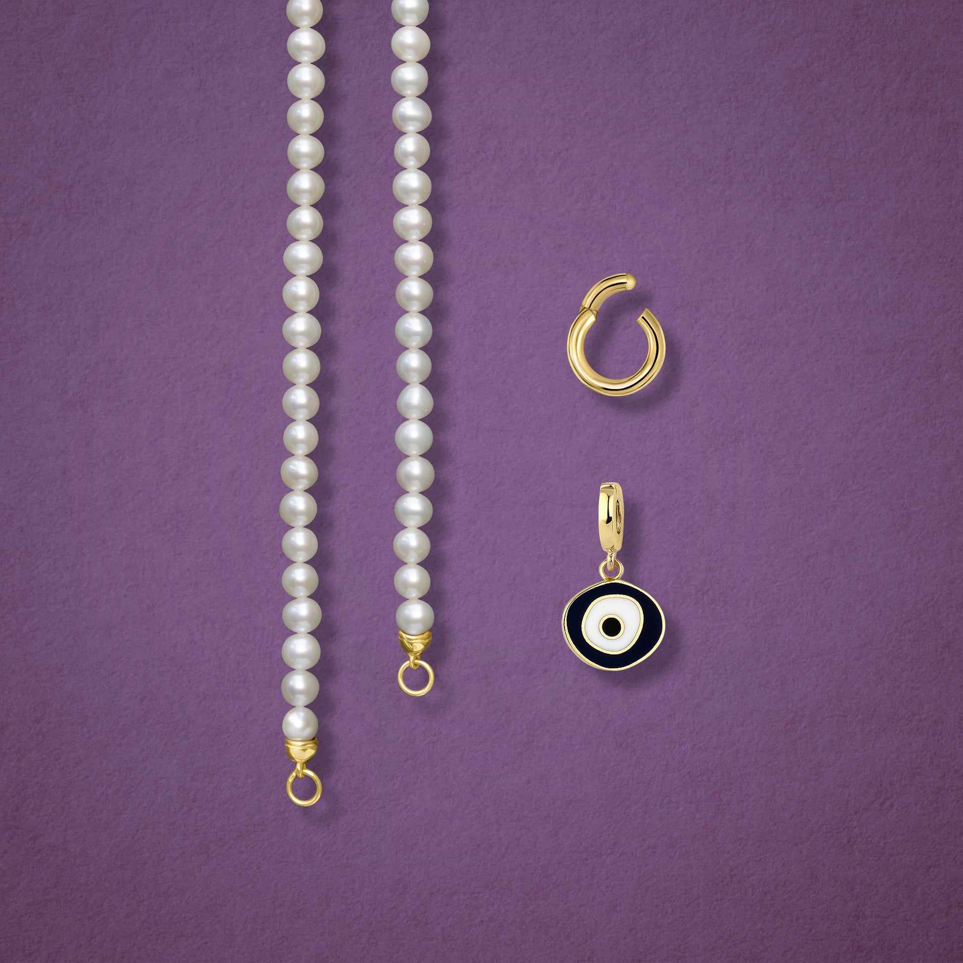 Close-up of the Obsidian Organic Evil Eye clip-on charm, Golden Link Charm Holder, and the Lustrous Pearl necklace displayed side by side on a pink background.