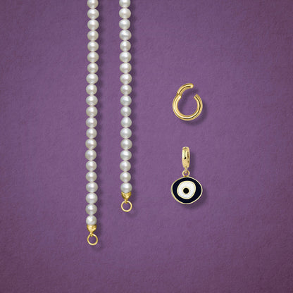 Close-up of the Obsidian Organic Evil Eye clip-on charm, Golden Link Charm Holder, and the Lustrous Pearl necklace displayed side by side on a pink background.