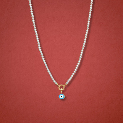 Sky Organic Evil Eye Charm, featuring blue, white, and black enamel, shown on the Lustrous Pearl necklace for scale against a red background.