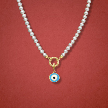 Close-up of the Sky Organic Evil Eye Charm with blue, white, and black enamel on the Lustrous Pearl necklace, shown on a red background.