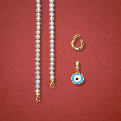 Close-up of the Sky Organic Evil Eye clip-on charm, Golden Link Charm Holder, and the Lustrous Pearl necklace displayed side by side on a red background.