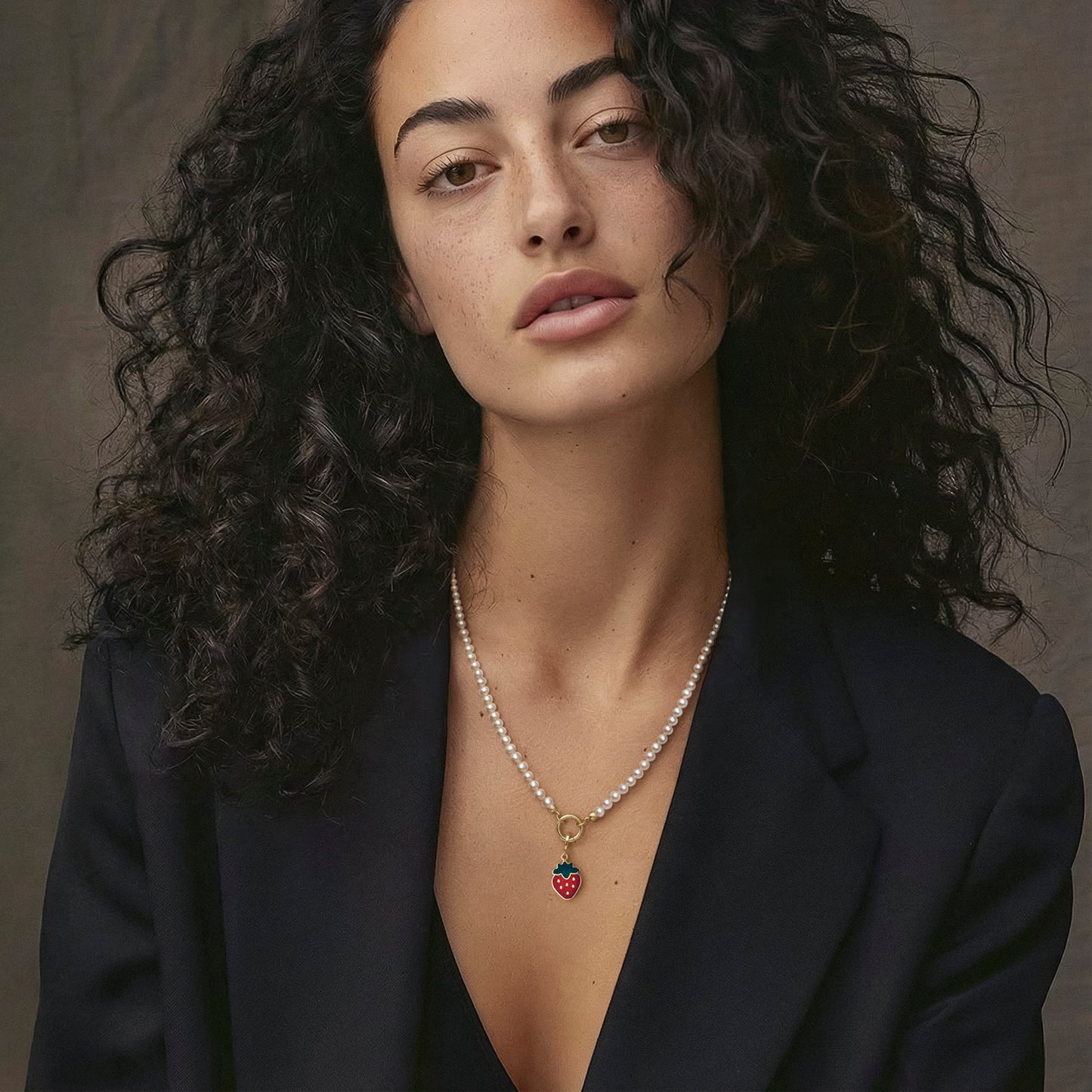 Model wearing the Lustrous Pearl Sweet Strawberry Charm Necklace, featuring a 20-inch strand of 3.5mm freshwater pearls, 14K solid gold clips, an 11mm outer diameter, a 1.5mm thick 14K solid gold charm holder, and a green and red enamel strawberry charm crafted in 14K solid gold.