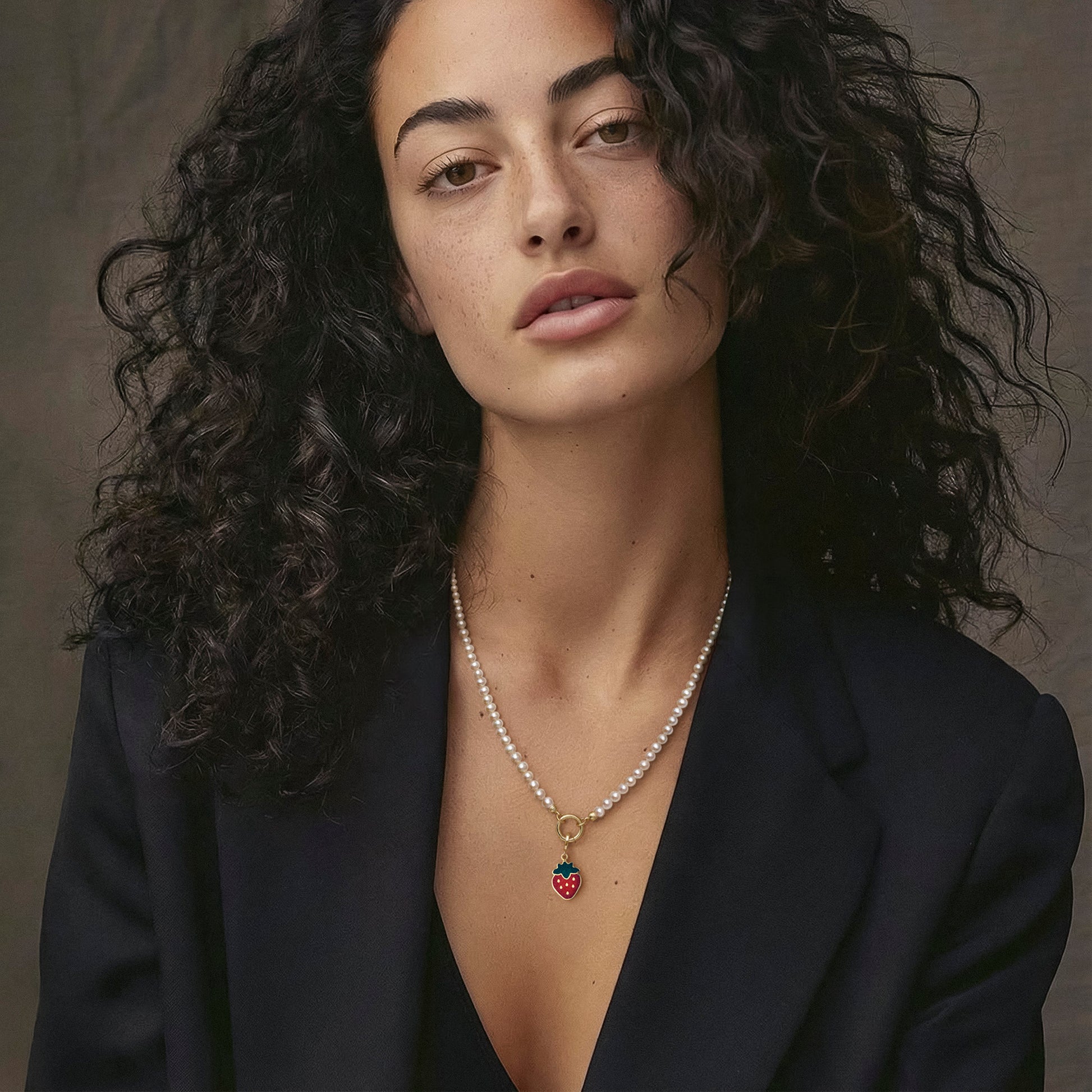 Model wearing the Lustrous Pearl Sweet Strawberry Charm Necklace, featuring a 20-inch strand of 3.5mm freshwater pearls, 14K solid gold clips, an 11mm outer diameter, a 1.5mm thick 14K solid gold charm holder, and a green and red enamel strawberry charm crafted in 14K solid gold.