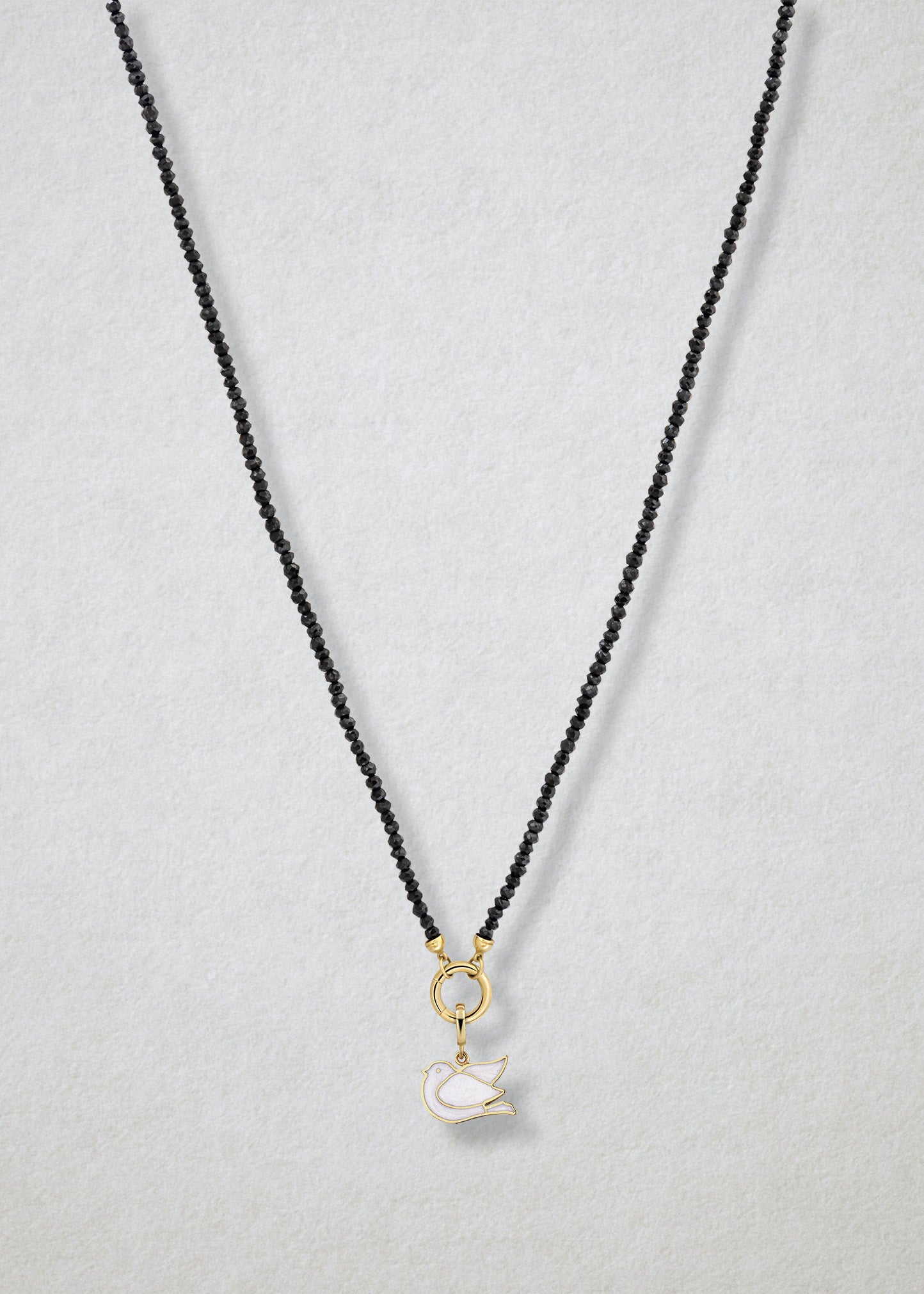 Noir Elegance Dove of Hope Charm Necklace in full view, showcasing faceted black spinel beads, a golden link charm holder, and dove of hope charm with white enamel by whywhy NYC.