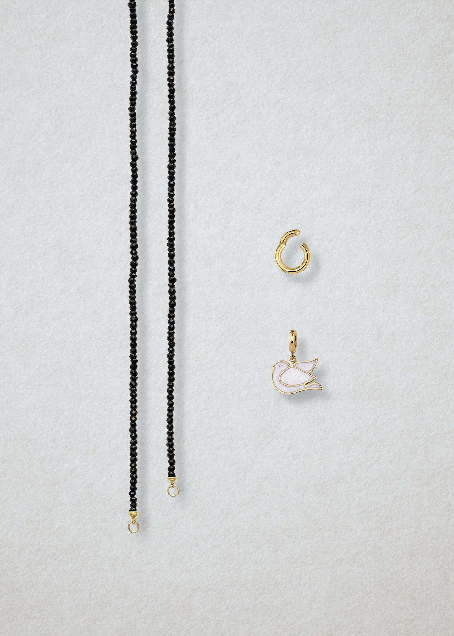 Separated components of the Noir Elegance Dove of Hope Charm Necklace, including black spinel necklace, golden link charm holder, and dove of hope charm with white enamel by whywhy NYC.