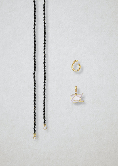 Separated components of the Noir Elegance Dove of Hope Charm Necklace, including black spinel necklace, golden link charm holder, and dove of hope charm with white enamel by whywhy NYC.