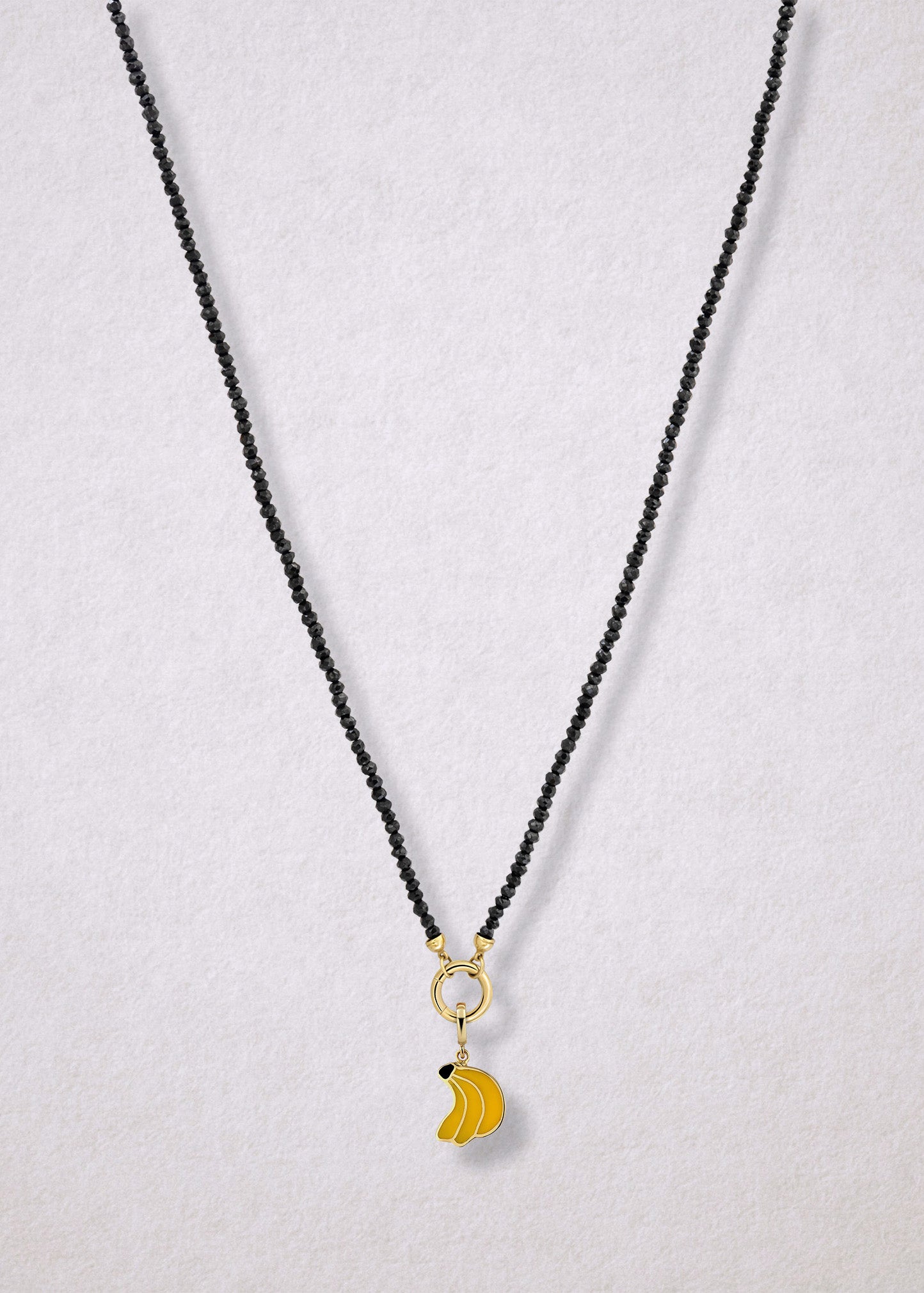 Noir Elegance Banana Bliss Charm Necklace in full view, showcasing faceted black spinel beads, a golden link charm holder, and banana bliss charm with yellow enamel by whywhy NYC.