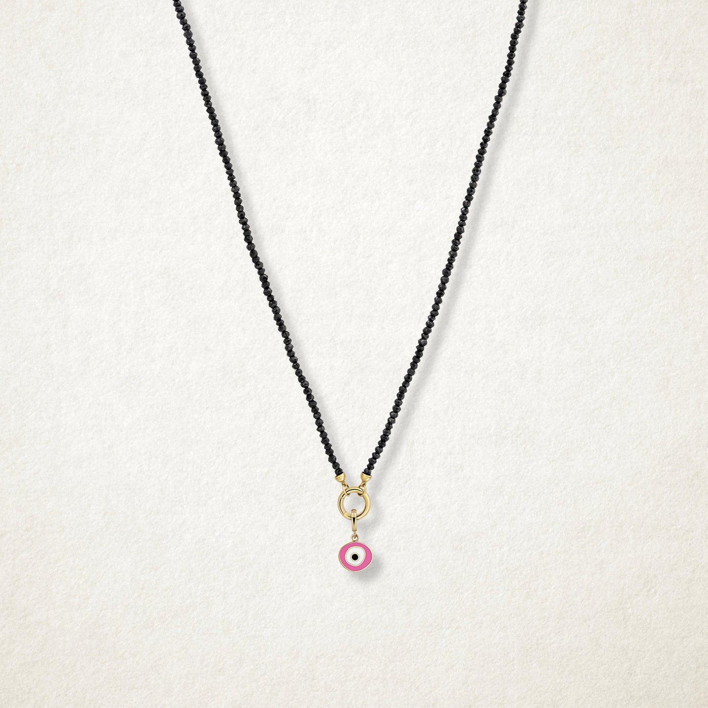 Blush Organic Evil Eye Charm with pink, white, and black enamel shown on the Noir Elegance black spinel necklace for scale on a soft light background.