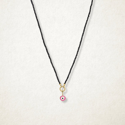 Blush Organic Evil Eye Charm with pink, white, and black enamel shown on the Noir Elegance black spinel necklace for scale on a soft light background.