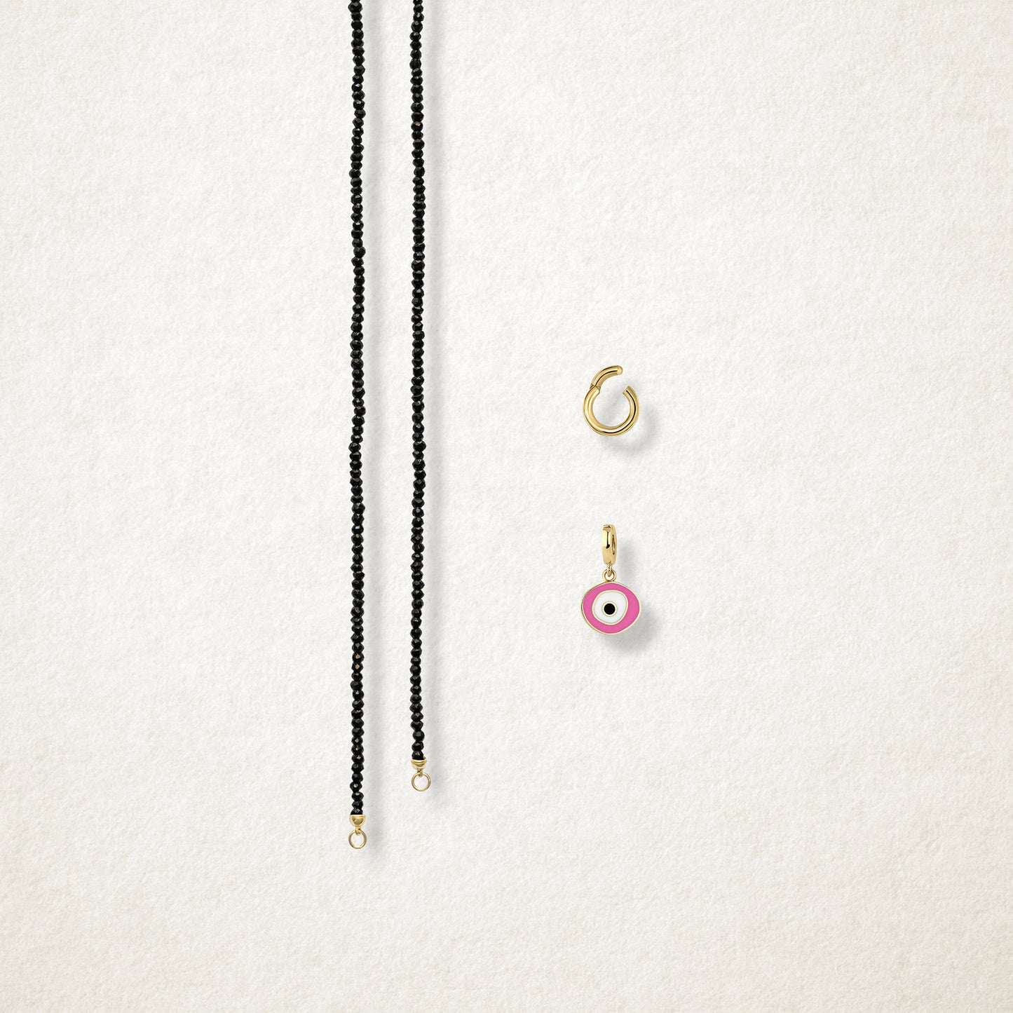 Blush Organic Evil Eye Charm and the Noir Elegance black spinel necklace displayed separately on a soft light background to show styling options.