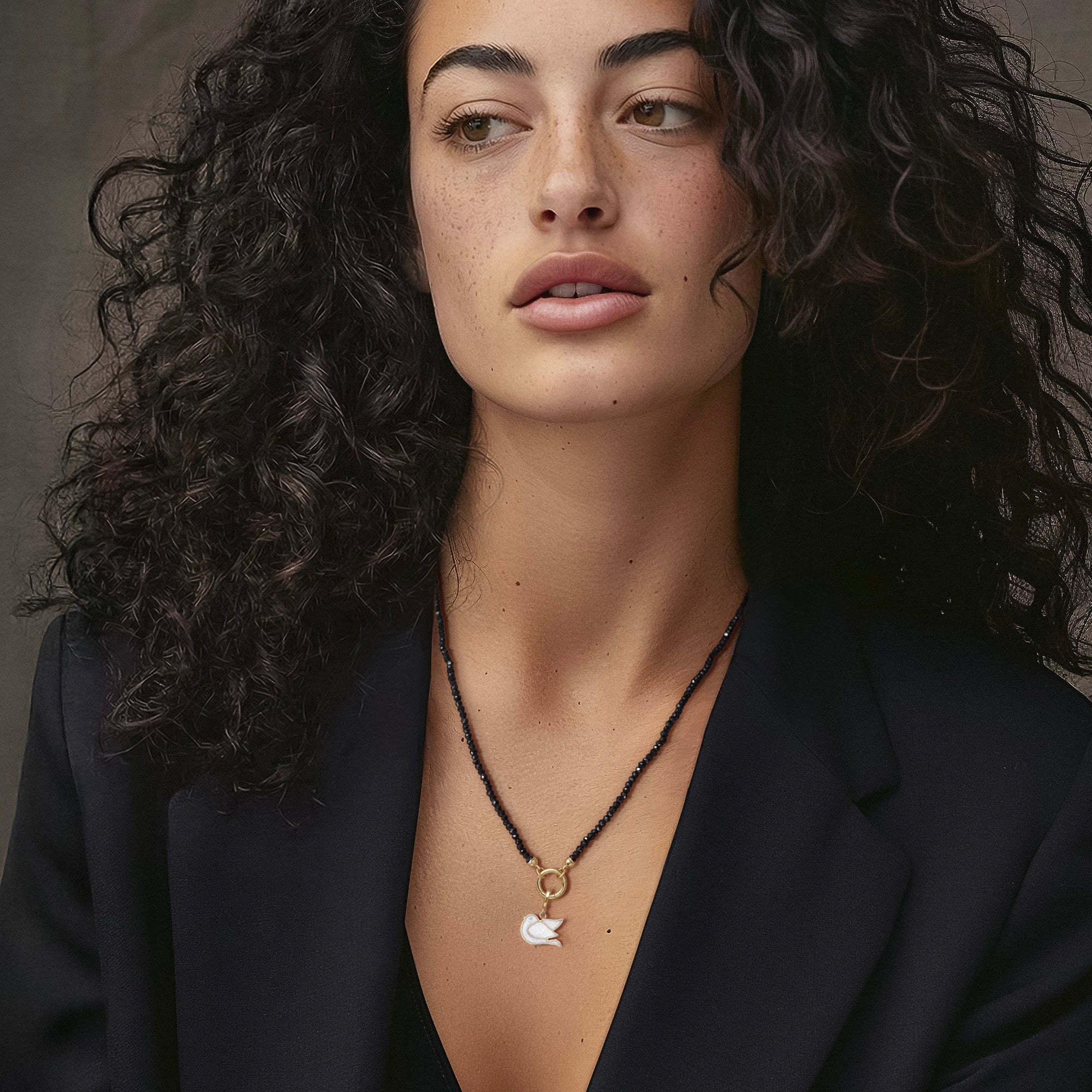 Model wearing the Noir Elegance Dove of Hope Charm Necklace, featuring 2mm black spinel beads, 14K solid gold clips, an 11mm outer diameter, a 1.5mm thick 14K solid gold charm holder, and a white dove charm crafted in 14K solid gold.