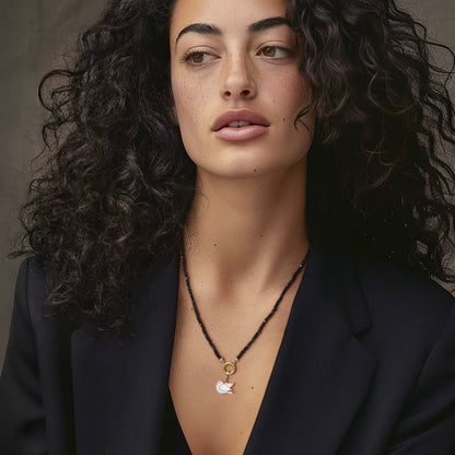 Model wearing the Noir Elegance Dove of Hope Charm Necklace, featuring 2mm black spinel beads, 14K solid gold clips, an 11mm outer diameter, a 1.5mm thick 14K solid gold charm holder, and a white dove charm crafted in 14K solid gold.