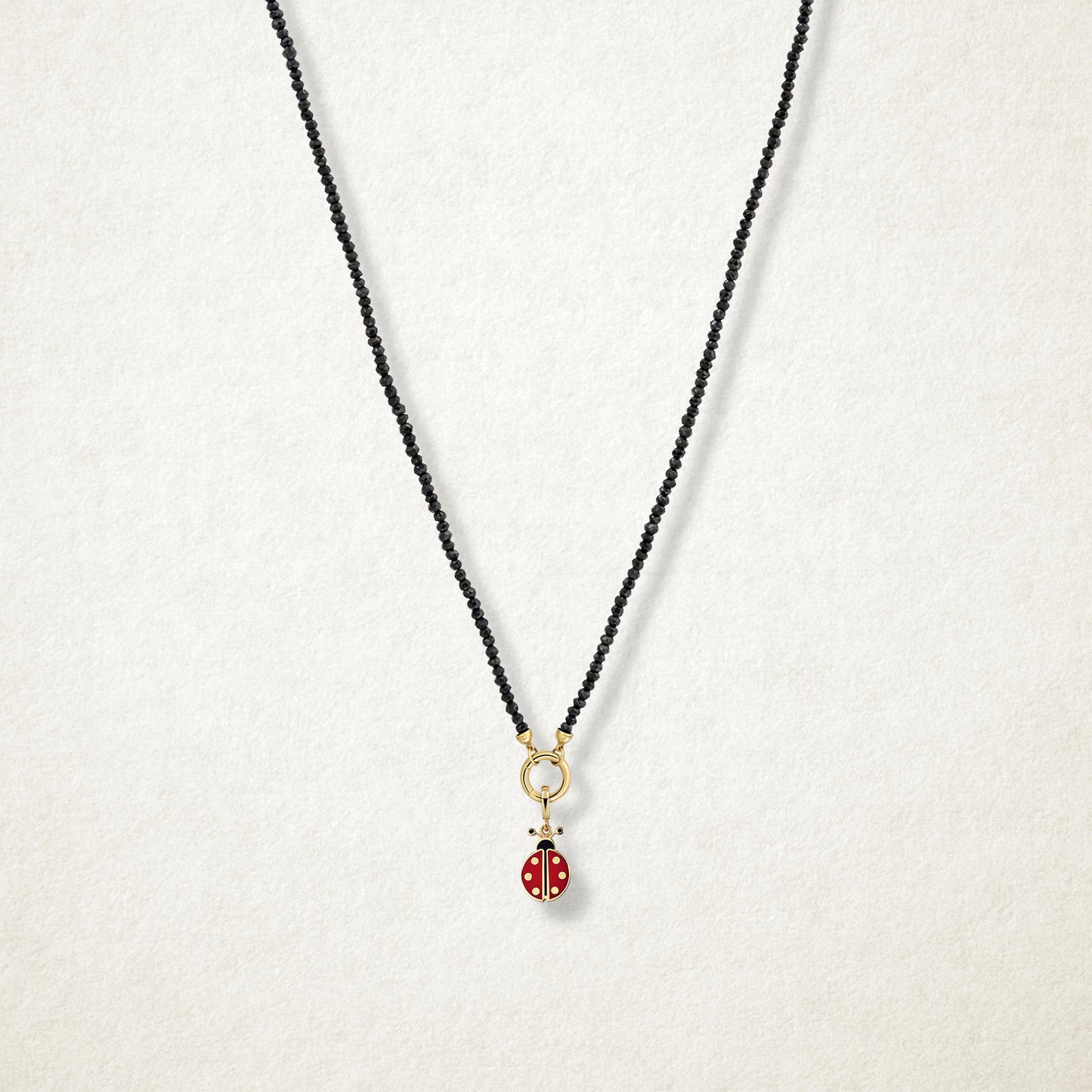 Lucky Ladybird Charm with red and black enamel shown on the Noir Elegance black spinel necklace for scale on a soft light background.