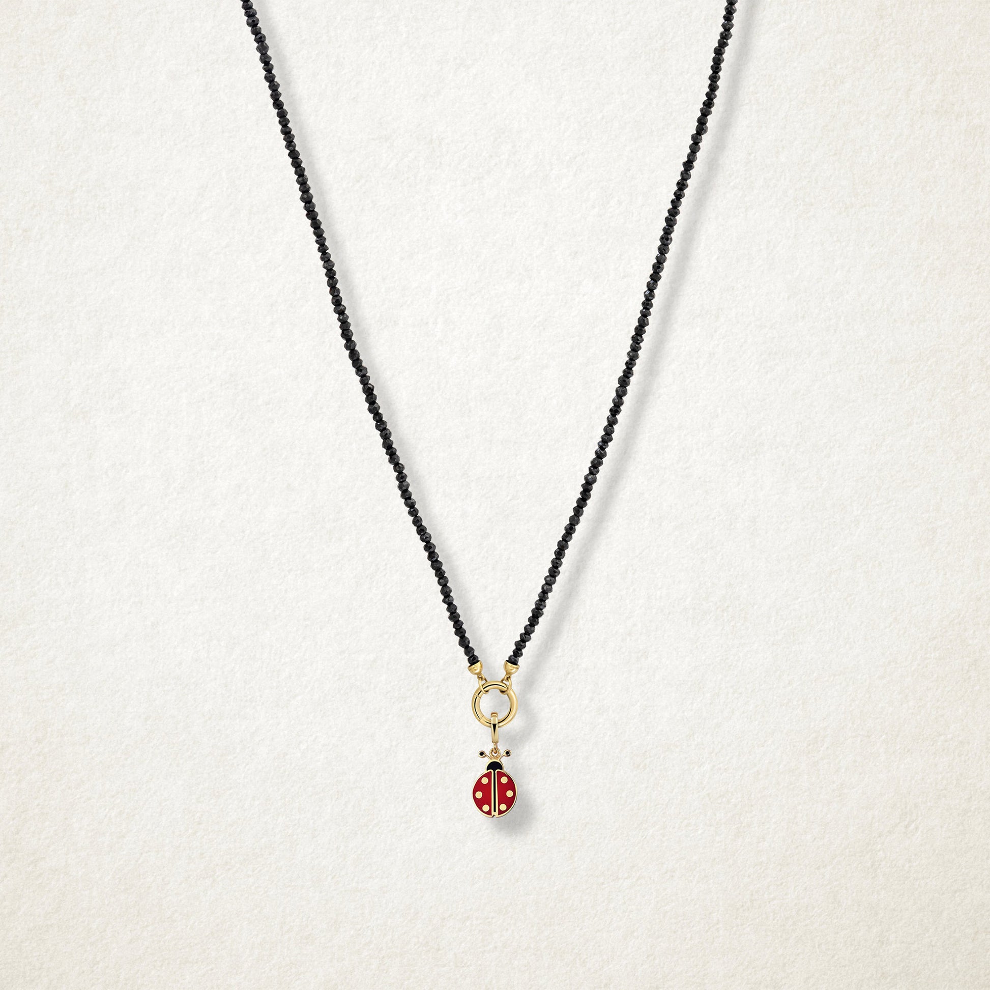 Lucky Ladybird Charm with red and black enamel shown on the Noir Elegance black spinel necklace for scale on a soft light background.