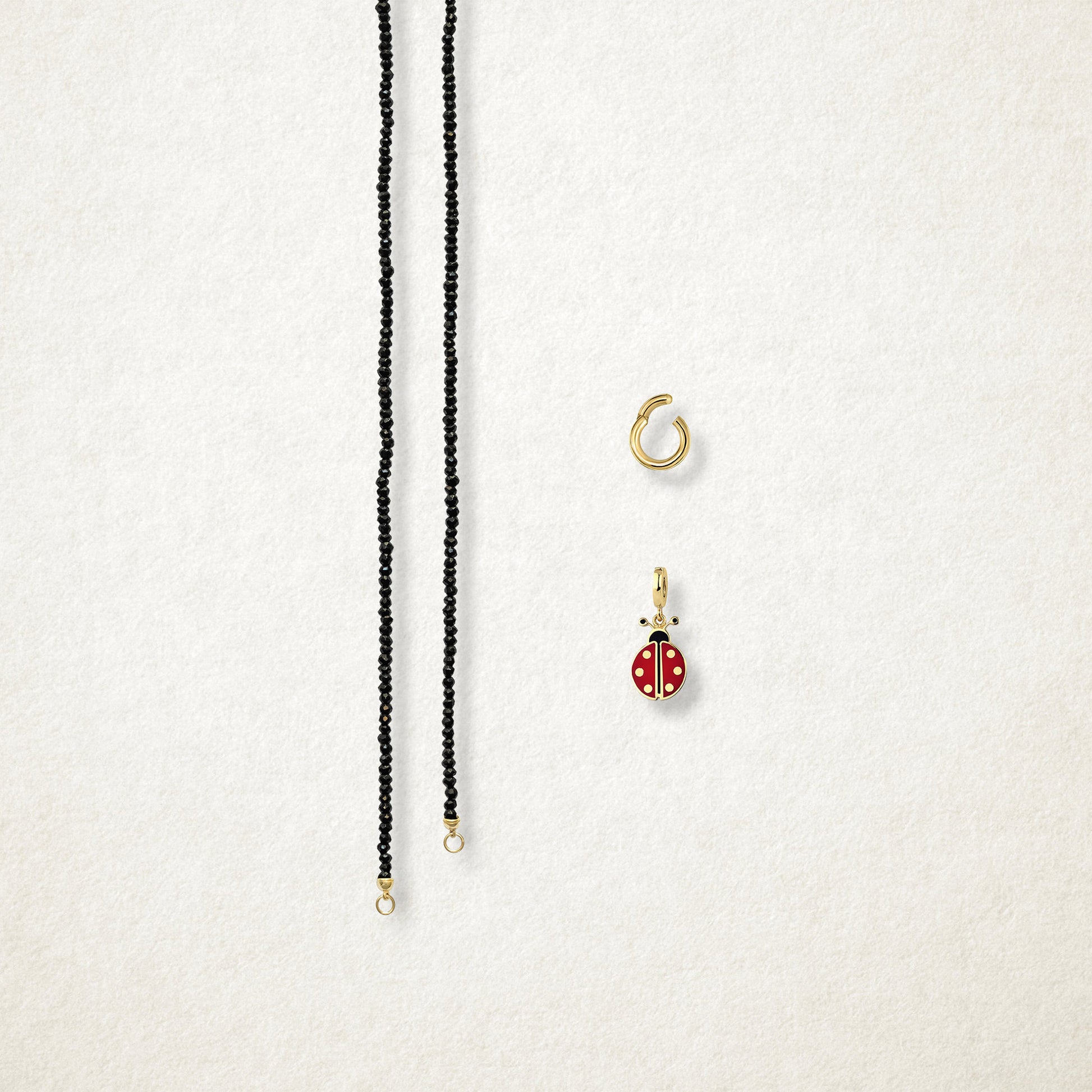 Lucky Ladybird Charm and the Noir Elegance black spinel necklace displayed separately on a soft light background to show styling options.