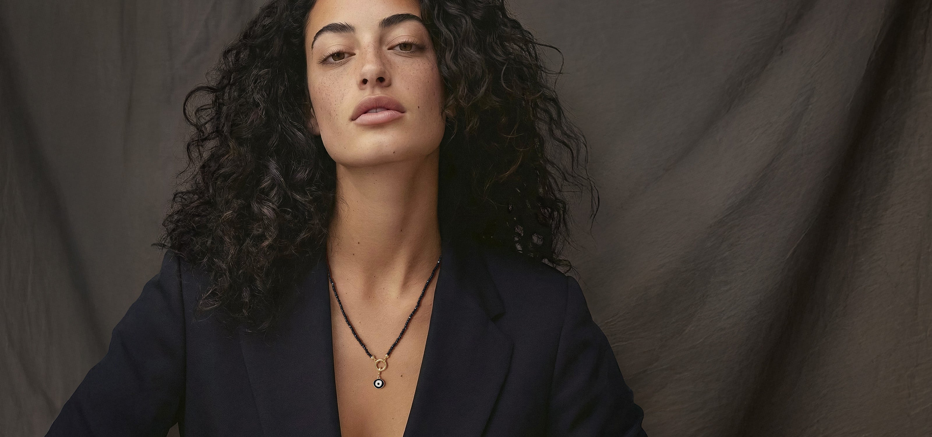 Model wearing the Noir Elegance Obsidian Organic Evil Eye Necklace, featuring black spinel beads and a 14K solid gold evil eye charm, styled for modern everyday elegance.