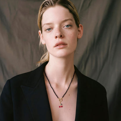 Blonde model wearing the Noir Elegance Cherry on Top charm necklace featuring a 14K solid gold cherry enamel charm on a black spinel bead necklace.