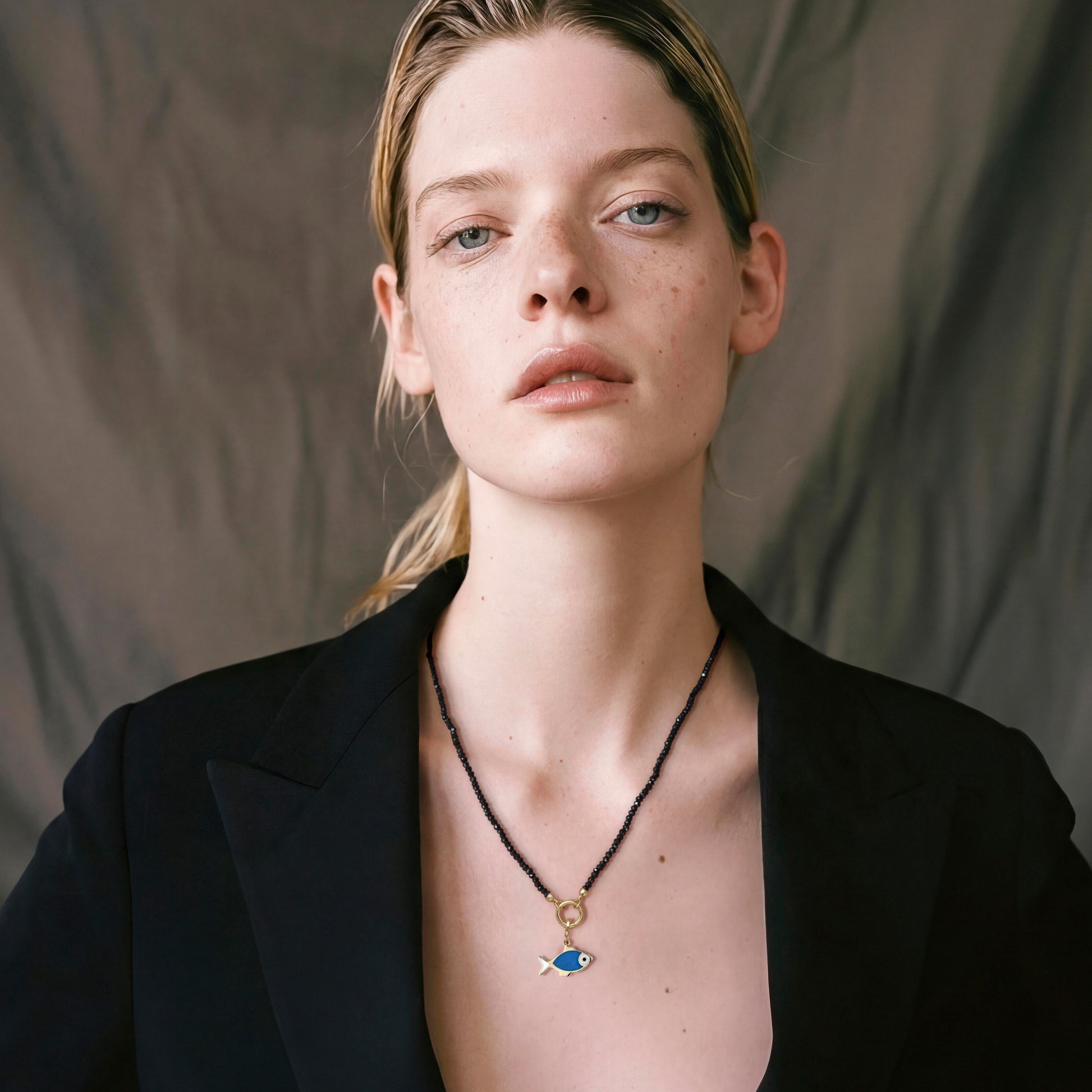 Blonde model wearing the Noir Elegance Fishy Wishes charm necklace featuring a 14K solid gold fish enamel charm on a black spinel bead necklace.