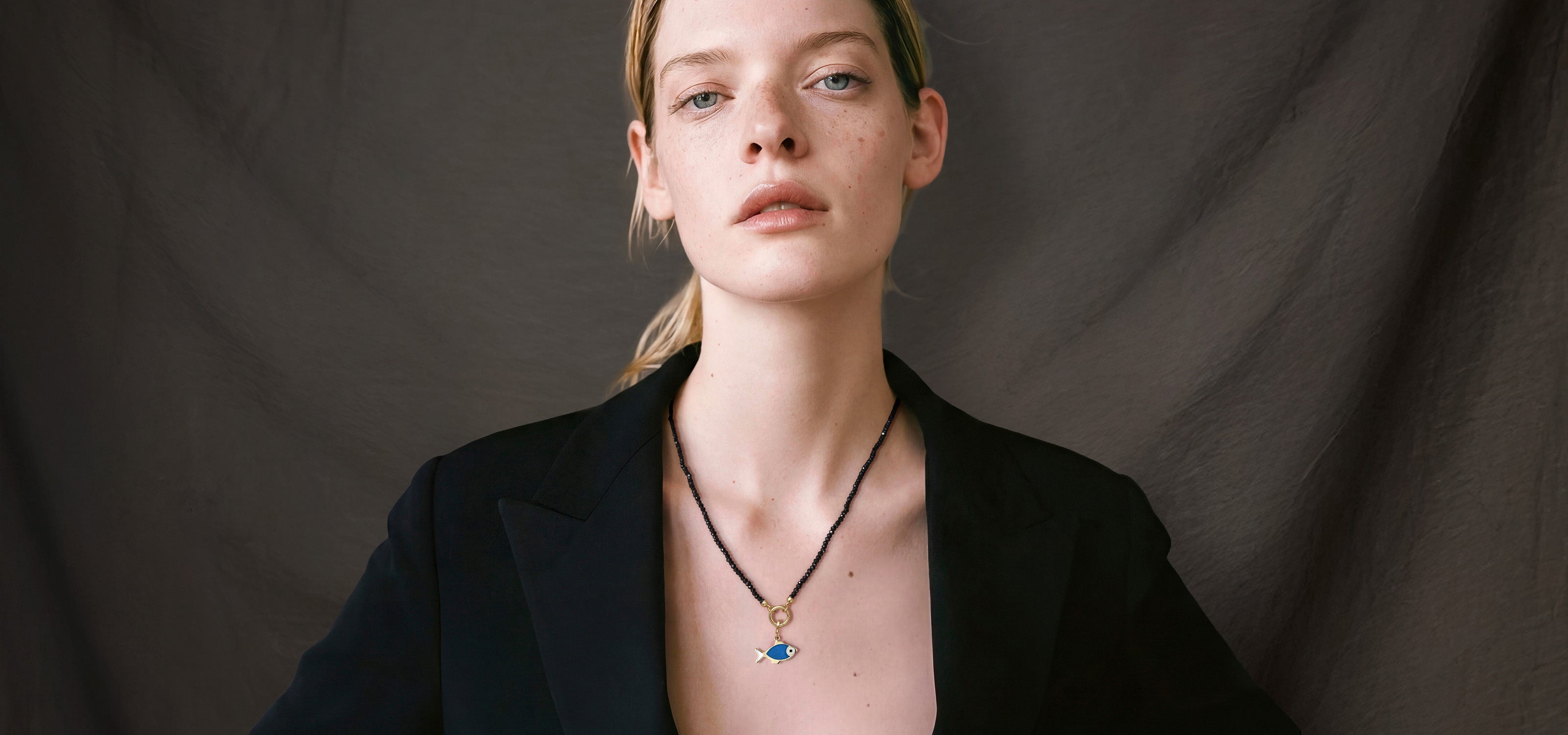 Blonde model wearing the Noir Elegance Fishy Wishes charm necklace featuring a 14K solid gold fish enamel charm on a black spinel bead necklace.