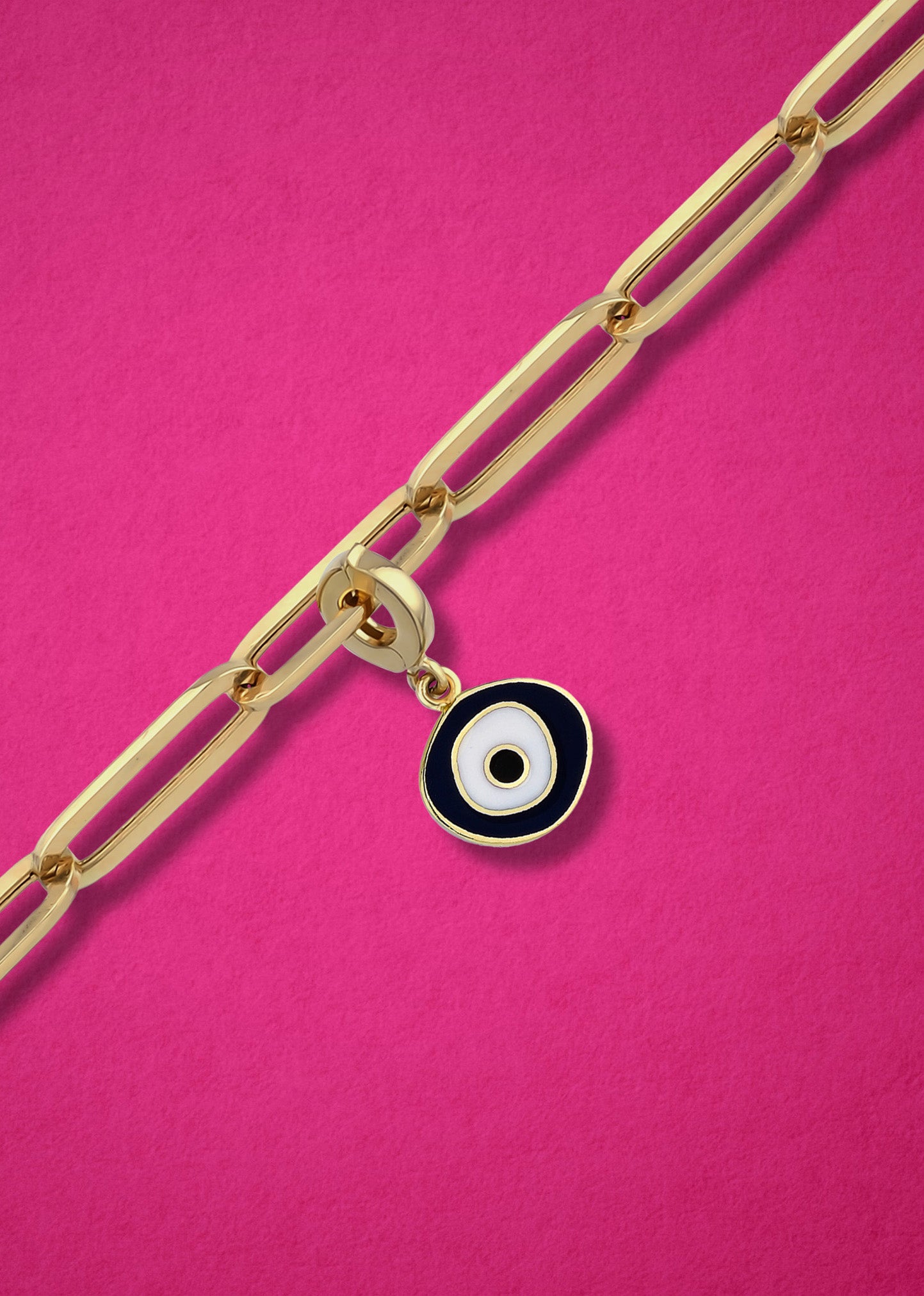 Obsidian Organic Evil Eye clip-on charm crafted in 14K solid gold with black and white enamel, shown hanging on a gold chain on a magenta background.