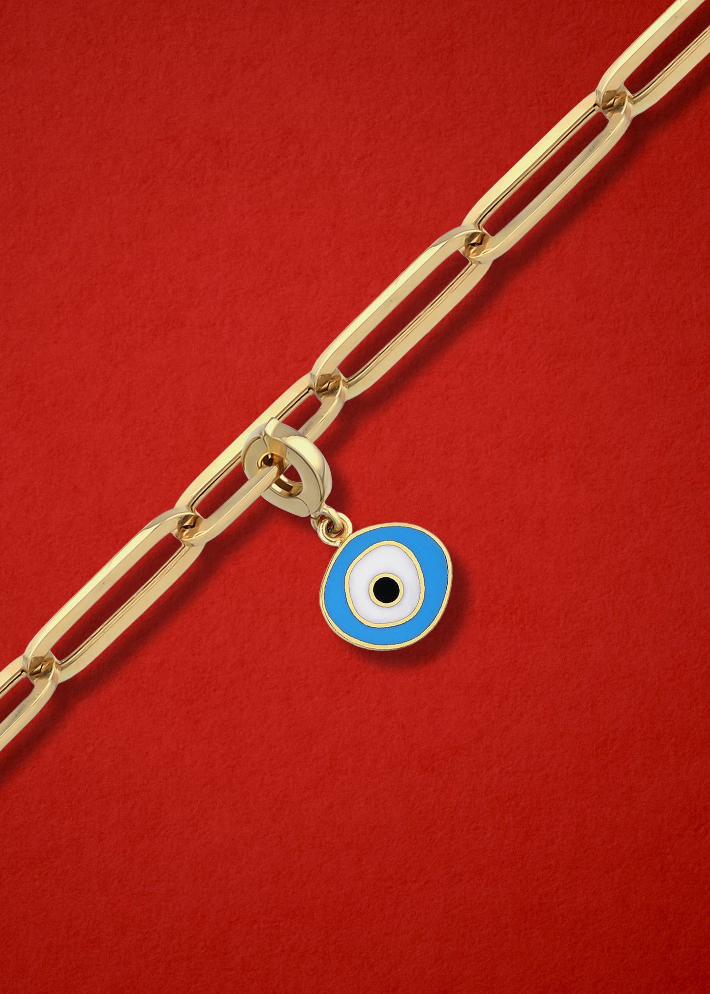Sky Organic Evil Eye clip-on charm crafted in 14K solid gold with sky blue, white, and black enamel, shown hanging on a gold chain on a red background.