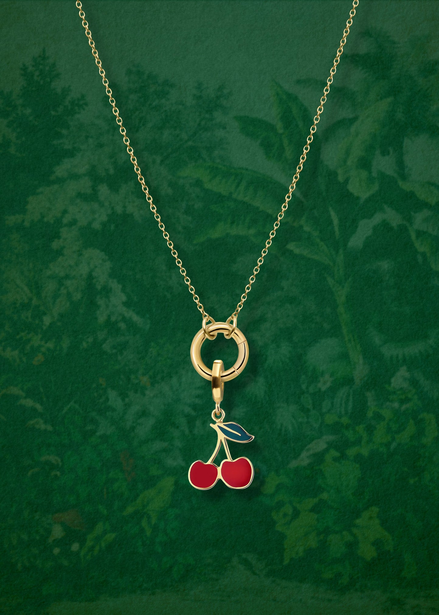 Close-up of the Golden Grace Cherry on Top Charm Necklace on a wallpaper background, featuring a 14K solid gold cable chain, a golden link charm holder, and a cherry on top charm with red enamel by whywhy NYC.